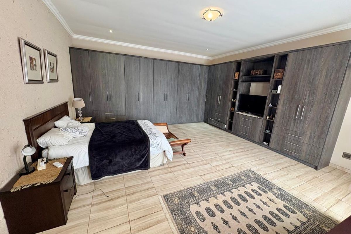 Spacious bedroom featuring extensive built-in cabinetry with integrated shelving and media storage, complemented by tiled flooring and crown molding.