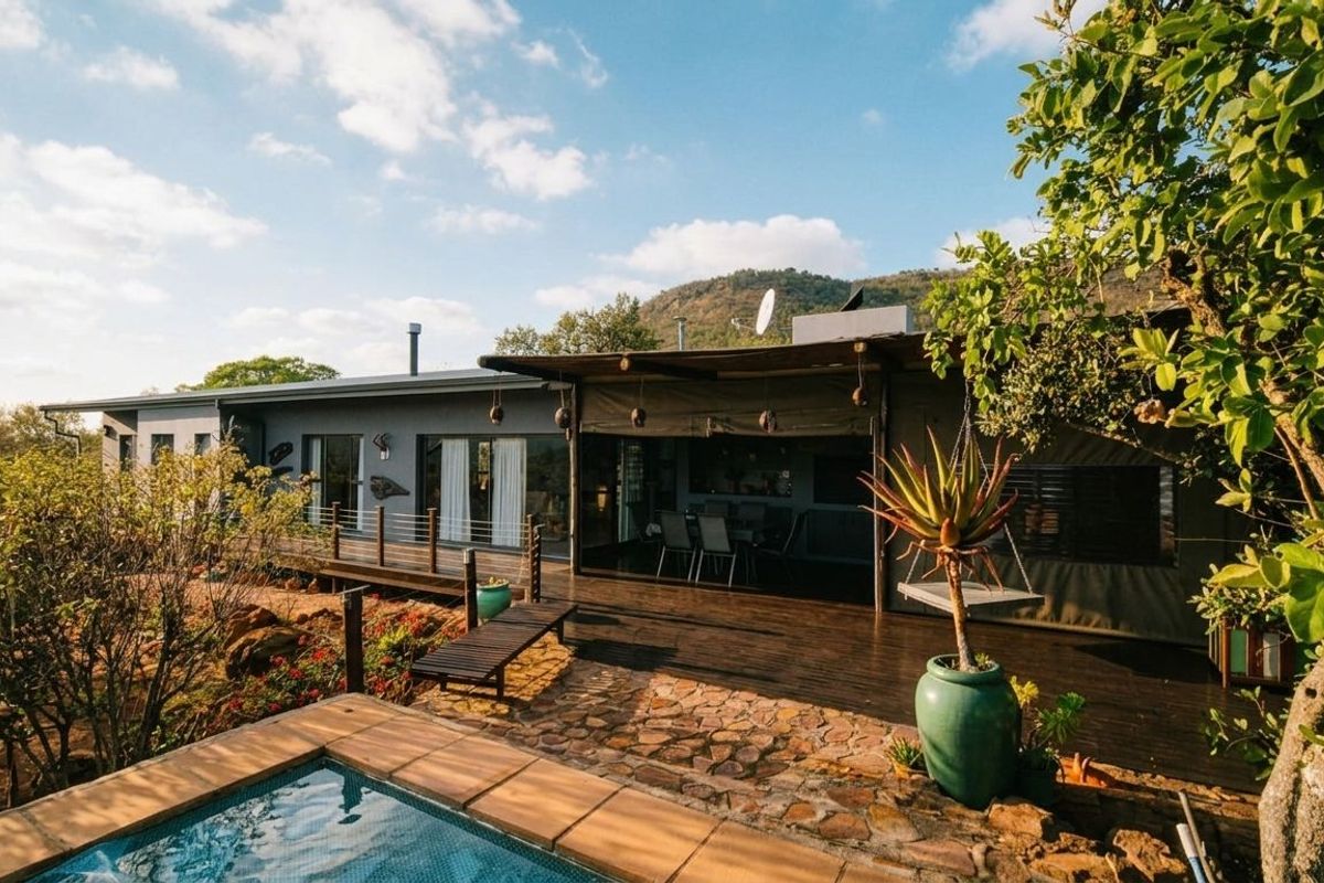 Rear exterior view featuring a swimming pool, expansive wooden decking, and a covered patio area overlooking the natural landscape.