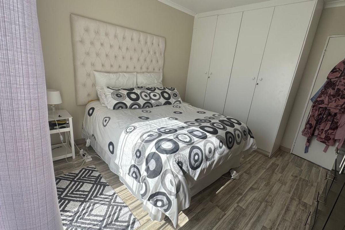 A functional bedroom featuring light-toned laminate flooring and ample built-in cupboard storage.