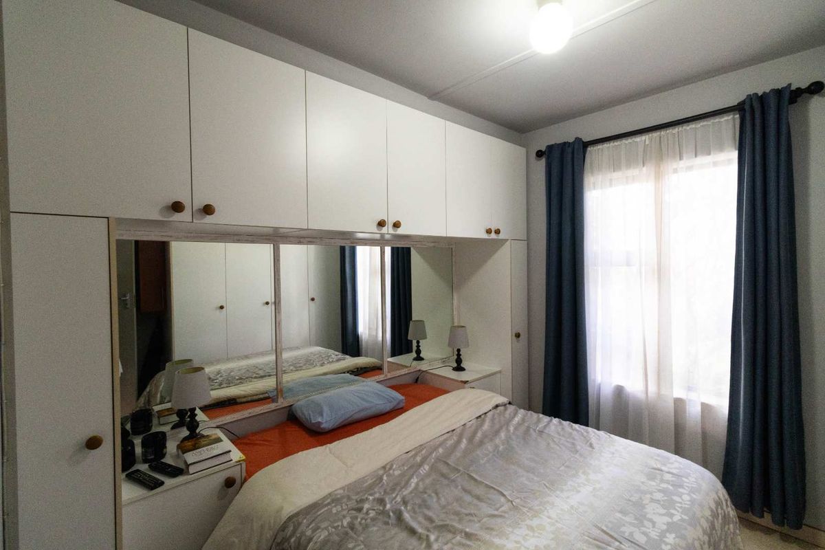 A bedroom featuring extensive built-in white cabinetry with an integrated mirrored headboard section and window with curtain rod.