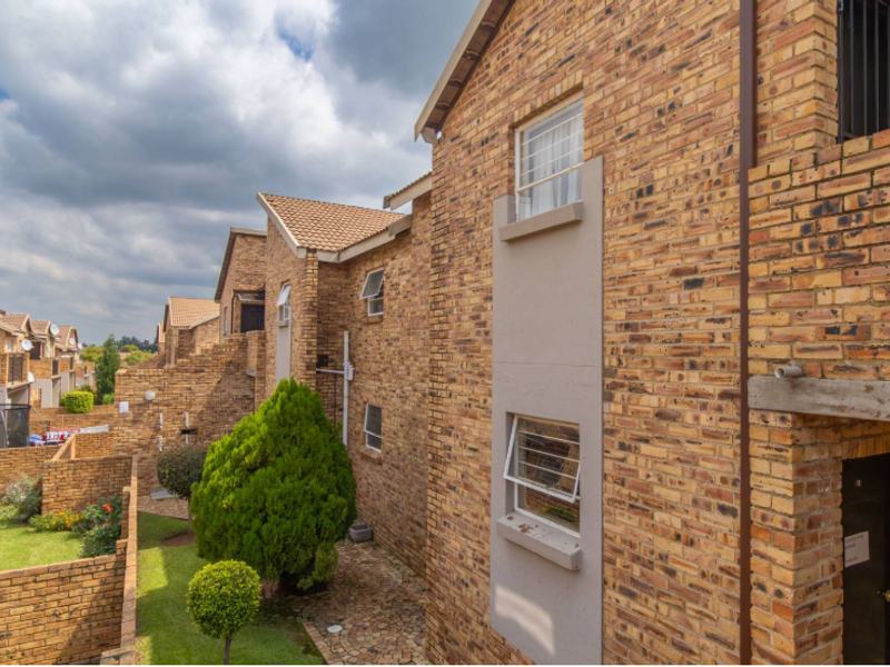 Rear view of a face brick apartment complex featuring a shared garden area, paved pathways, and secure window fittings.