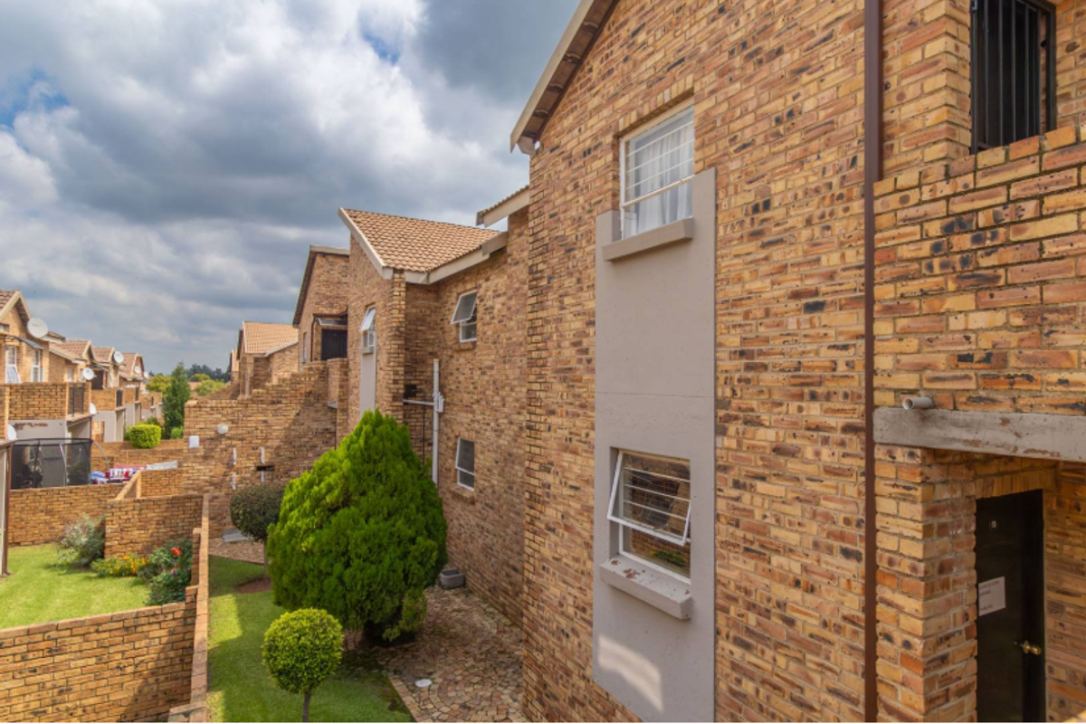Rear view of a face brick apartment complex featuring a shared garden area, paved pathways, and secure window fittings.