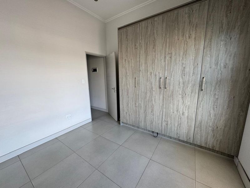 A clean, empty bedroom featuring modern wood-look built-in cupboards and neutral tiled flooring, offering a versatile space ready for personalization.