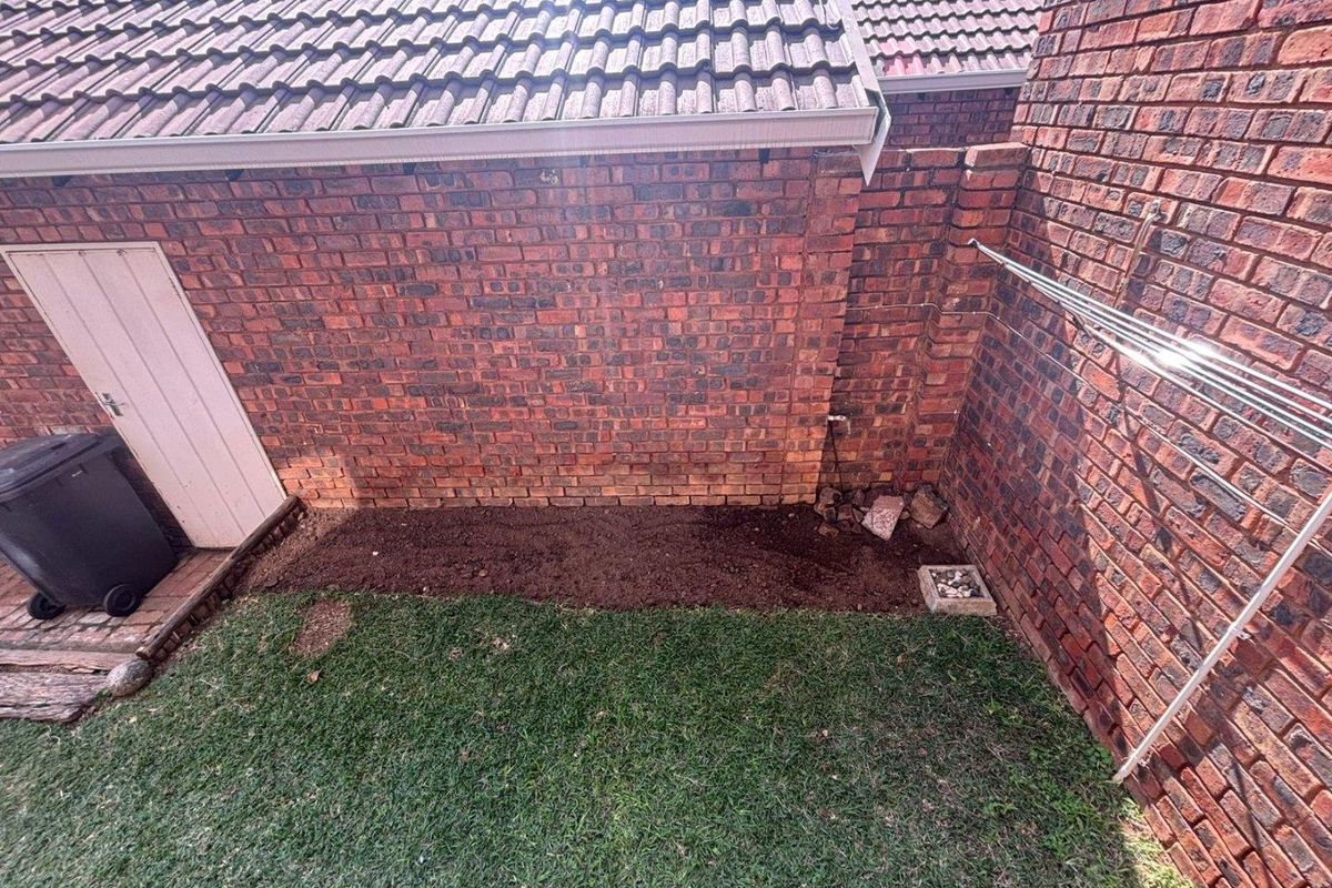 A private rear courtyard area featuring exposed brick walls, a tiled roof overhang, and a small grassed section with a wall-mounted washing line.