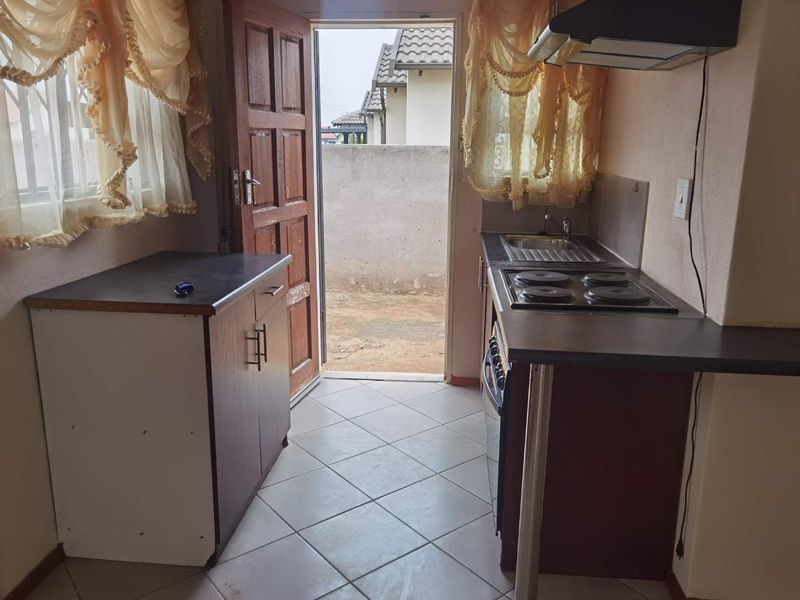 Compact kitchen featuring built-in cabinetry, electric hob, extractor fan, and direct access to the rear exterior area.