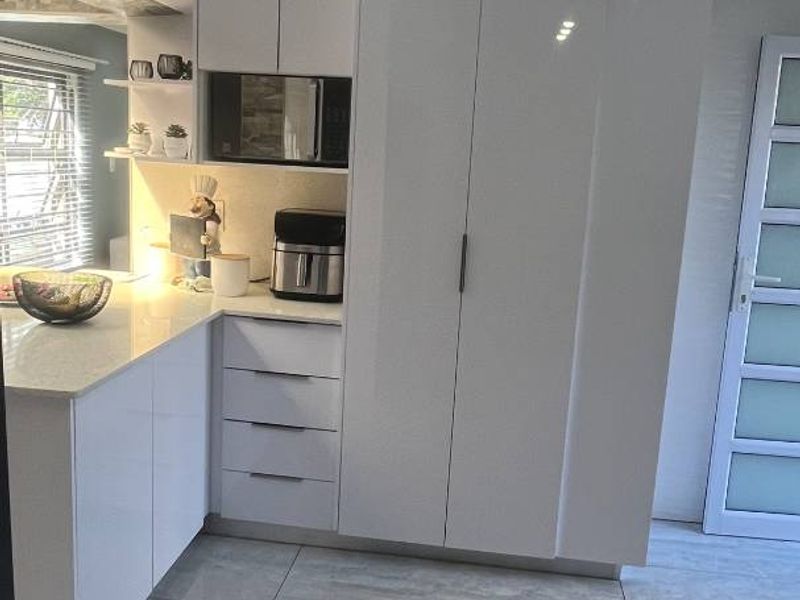 Modern kitchen featuring sleek white high-gloss cabinetry, stone countertops, built-in microwave, and large format polished floor tiles.