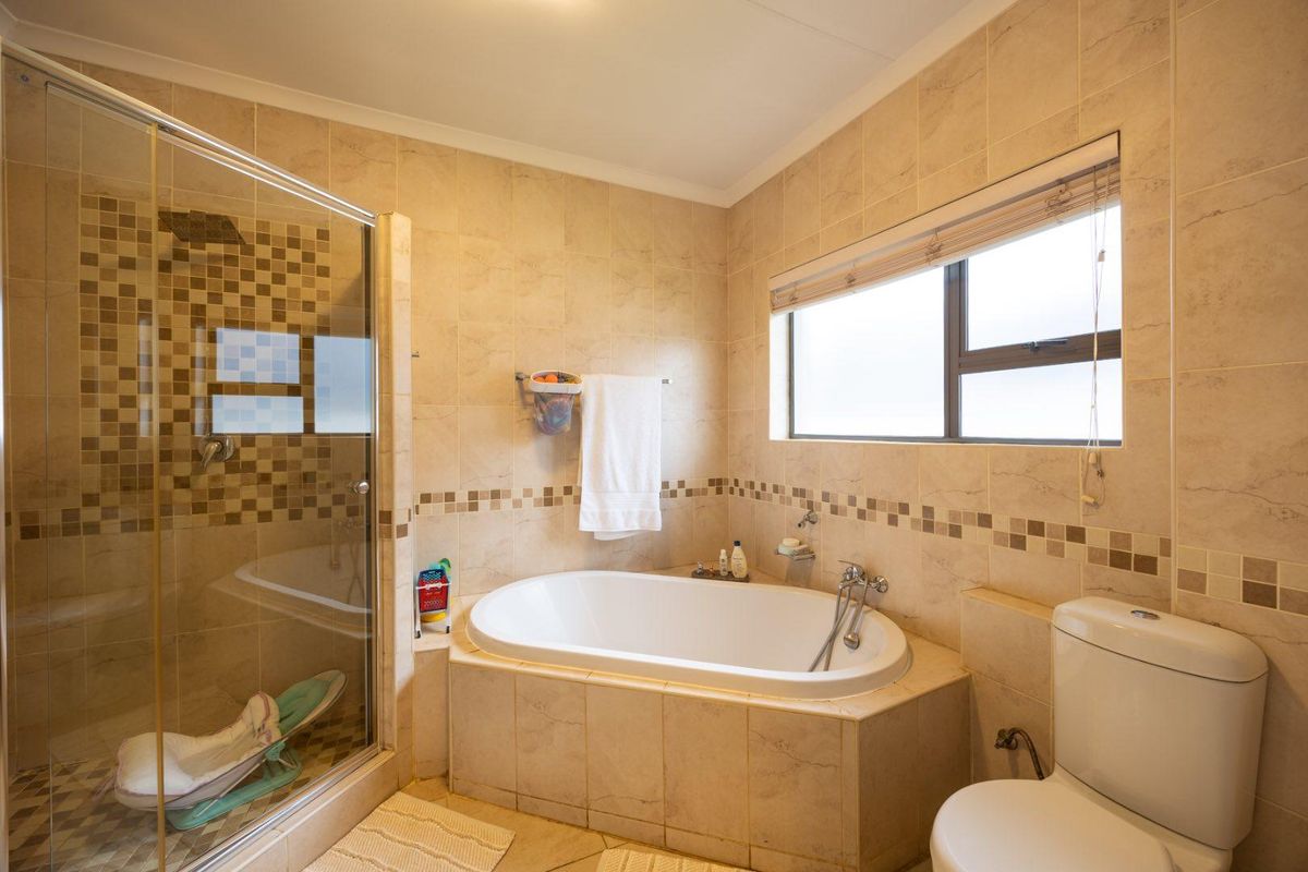 A well-maintained bathroom featuring a glass-enclosed shower, a built-in bathtub, and neutral ceramic tiling throughout.