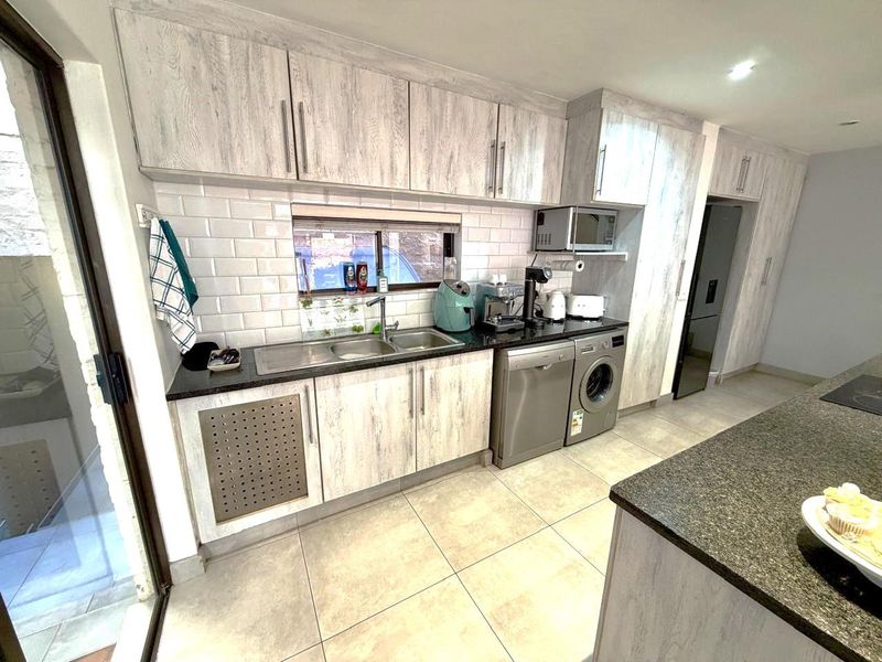Modern kitchen featuring light wood-grain cabinetry, granite countertops, subway tile backsplash, and integrated space for laundry appliances.