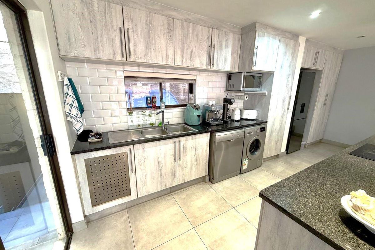 Modern kitchen featuring light wood-grain cabinetry, granite countertops, subway tile backsplash, and integrated space for laundry appliances.