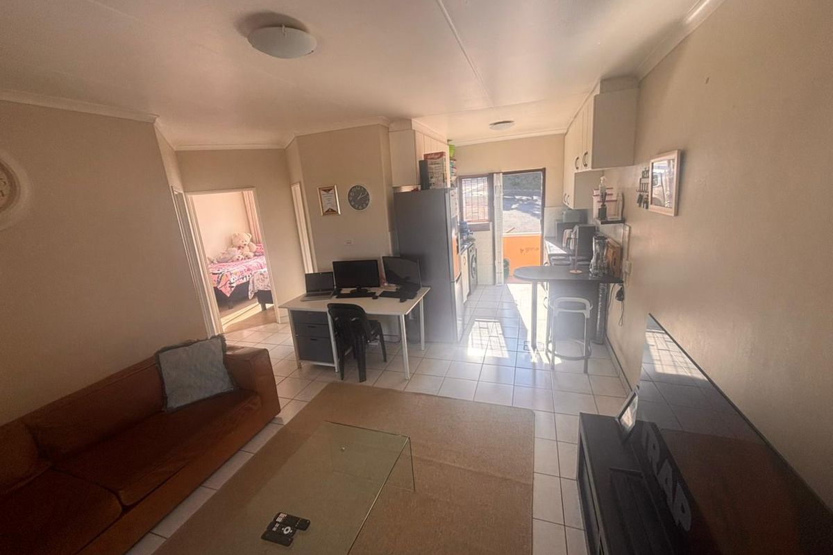 Open-plan living area featuring tiled flooring, a compact kitchen space with built-in cabinetry, and direct access to an outdoor area.