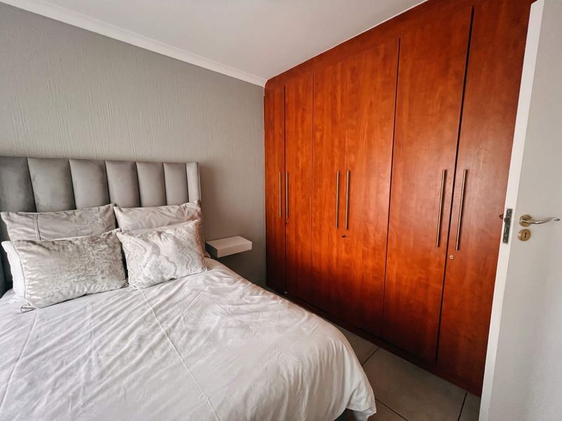 A well-maintained bedroom featuring extensive floor-to-ceiling built-in wooden cupboards and neutral tiled flooring.