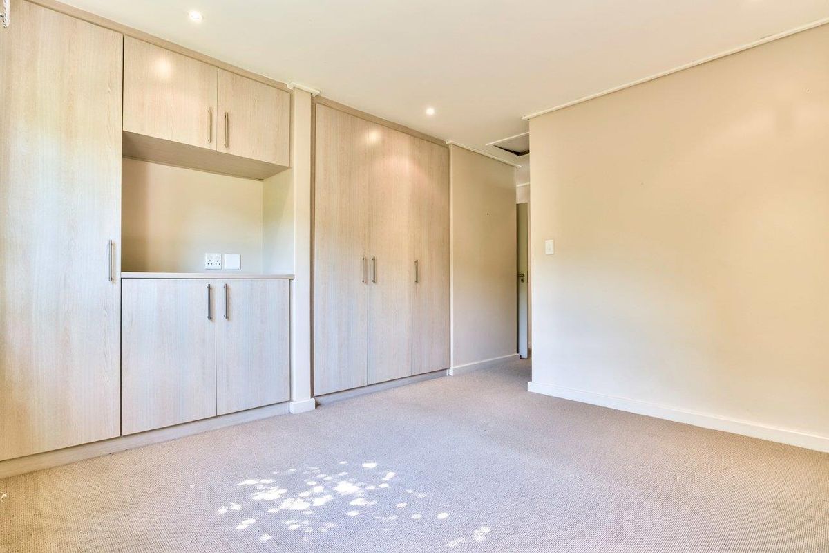A bright, empty bedroom featuring neutral-toned built-in cabinetry, recessed downlighting, and clean carpet flooring, offering a versatile space for residents.