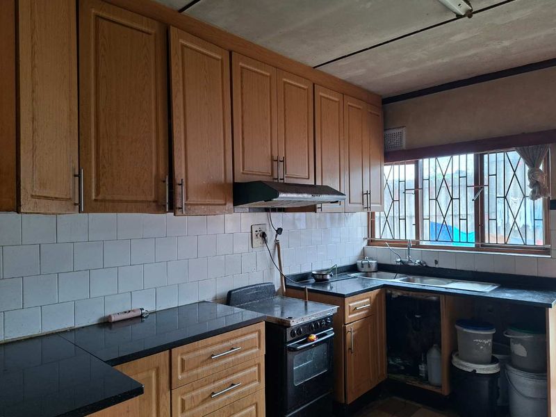 A dated kitchen featuring wooden cabinetry, black granite countertops, a tiled backsplash, and a stainless steel sink with security bars on the window.