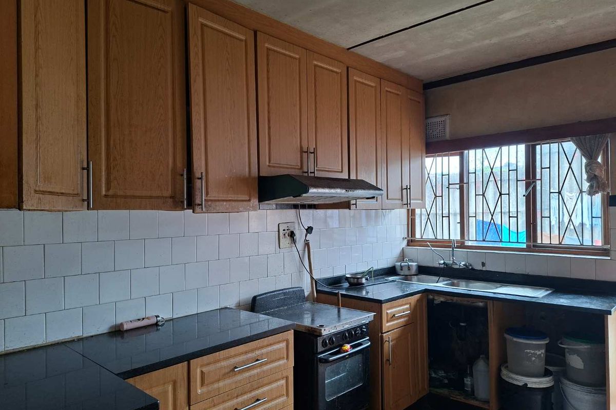 A dated kitchen featuring wooden cabinetry, black granite countertops, a tiled backsplash, and a stainless steel sink with security bars on the window.