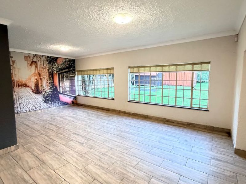 A spacious, empty living room featuring modern wood-look tiled flooring, large windows providing natural light, and a decorative wall mural.