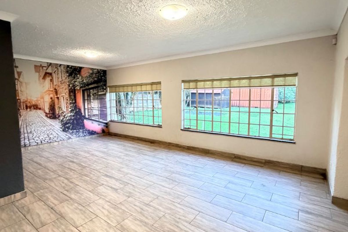 A spacious, empty living room featuring modern wood-look tiled flooring, large windows providing natural light, and a decorative wall mural.