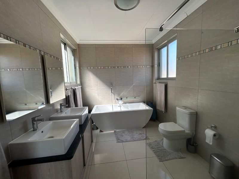 Modern bathroom featuring a double vanity, freestanding bathtub, glass shower screen, and neutral floor-to-ceiling tiling.