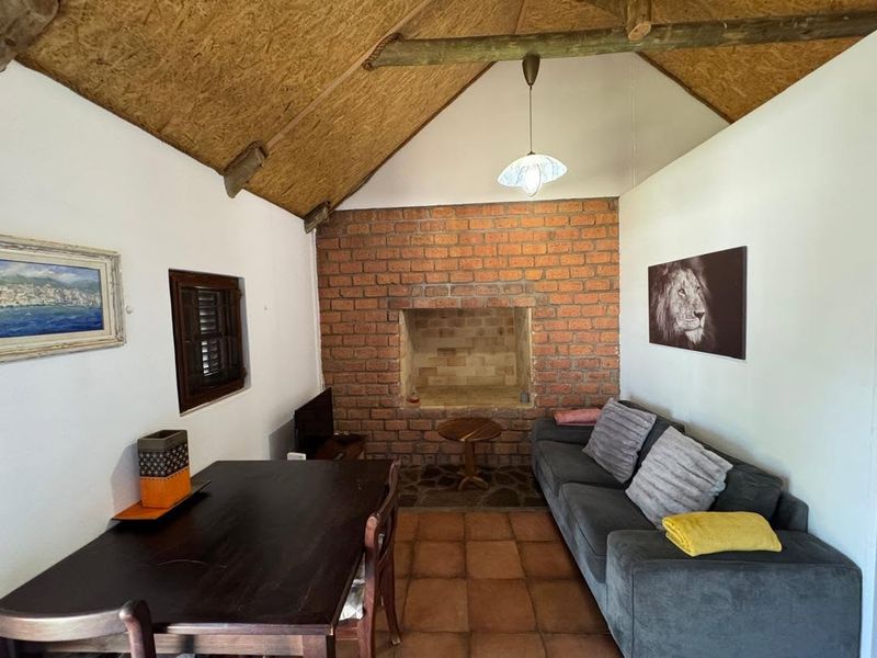Rustic living room featuring an exposed brick fireplace, vaulted ceiling with timber rafters, and terracotta floor tiles, creating a cozy, traditional atmosphere.