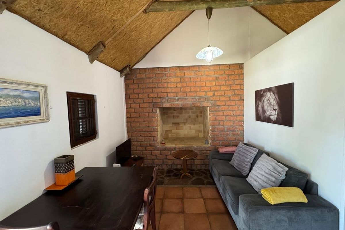 Rustic living room featuring an exposed brick fireplace, vaulted ceiling with timber rafters, and terracotta floor tiles, creating a cozy, traditional atmosphere.
