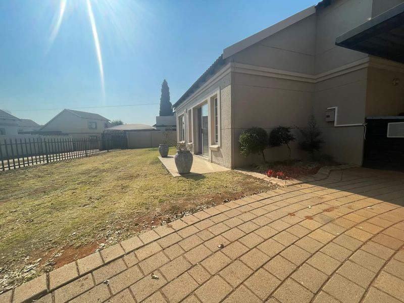 Rear exterior view of the property featuring a paved driveway, concrete patio area, and a fenced garden space.
