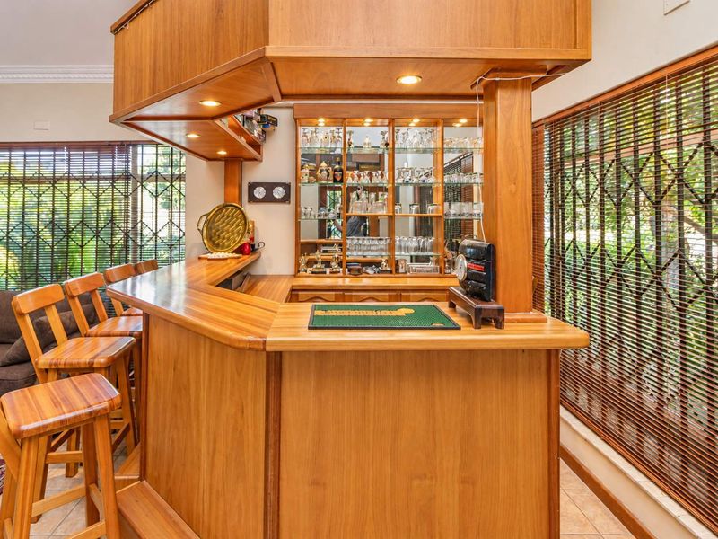 A dedicated home bar area featuring a custom-built wooden counter, overhead canopy with integrated lighting, and mirrored display shelving.