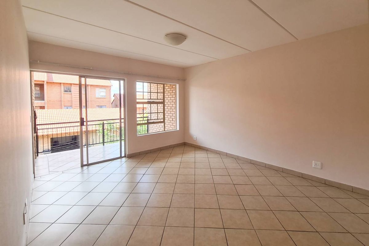 A bright, empty living area featuring tiled flooring, a ceiling light, and sliding glass doors that open onto a private balcony.