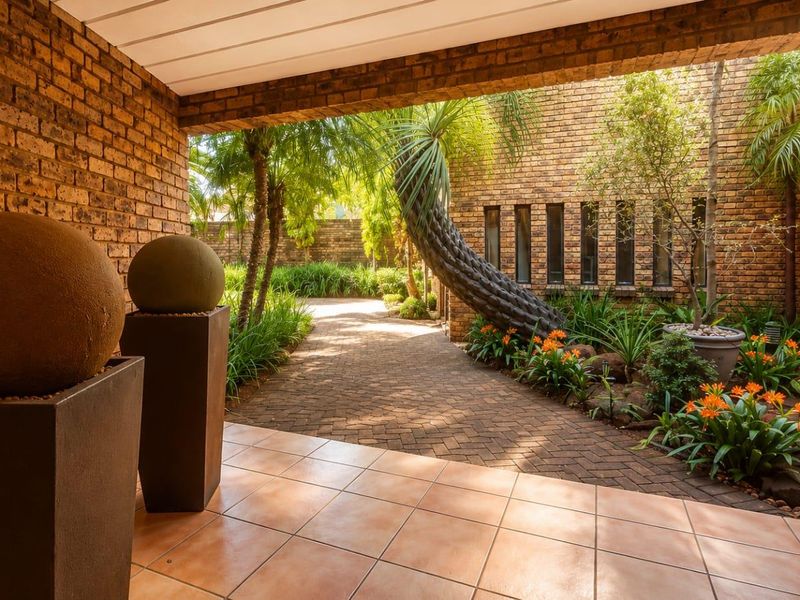 A covered patio area featuring exposed brick walls and tiled flooring, overlooking a landscaped garden with a paved walkway.