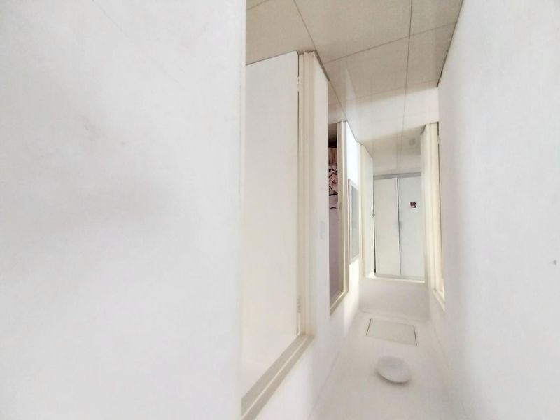 A narrow, minimalist hallway featuring a drop ceiling and built-in storage access points, finished in a neutral white palette.
