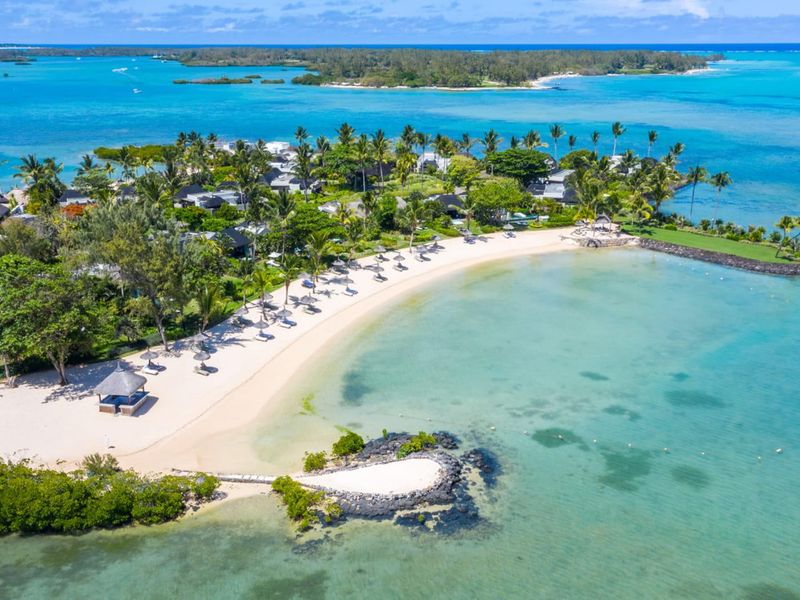 An expansive aerial view of a luxury coastal property featuring pristine sandy beaches, lush tropical landscaping, and direct access to turquoise lagoon waters.