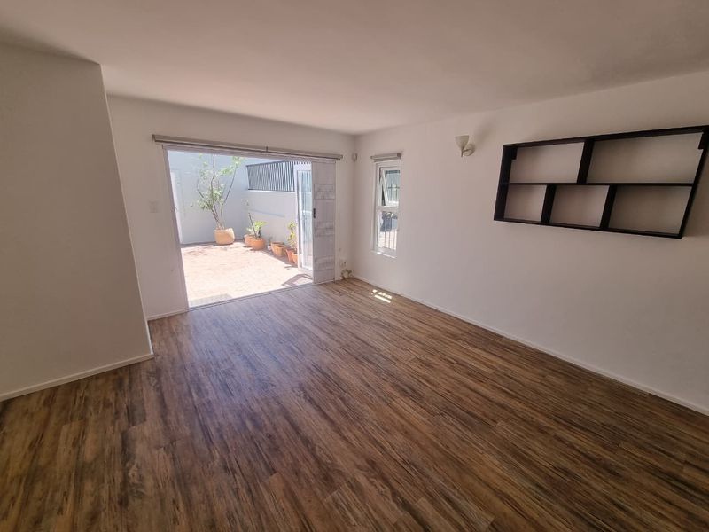 Bright and spacious living area featuring durable laminate flooring, built-in wall shelving, and direct access to an outdoor patio through sliding glass doors.