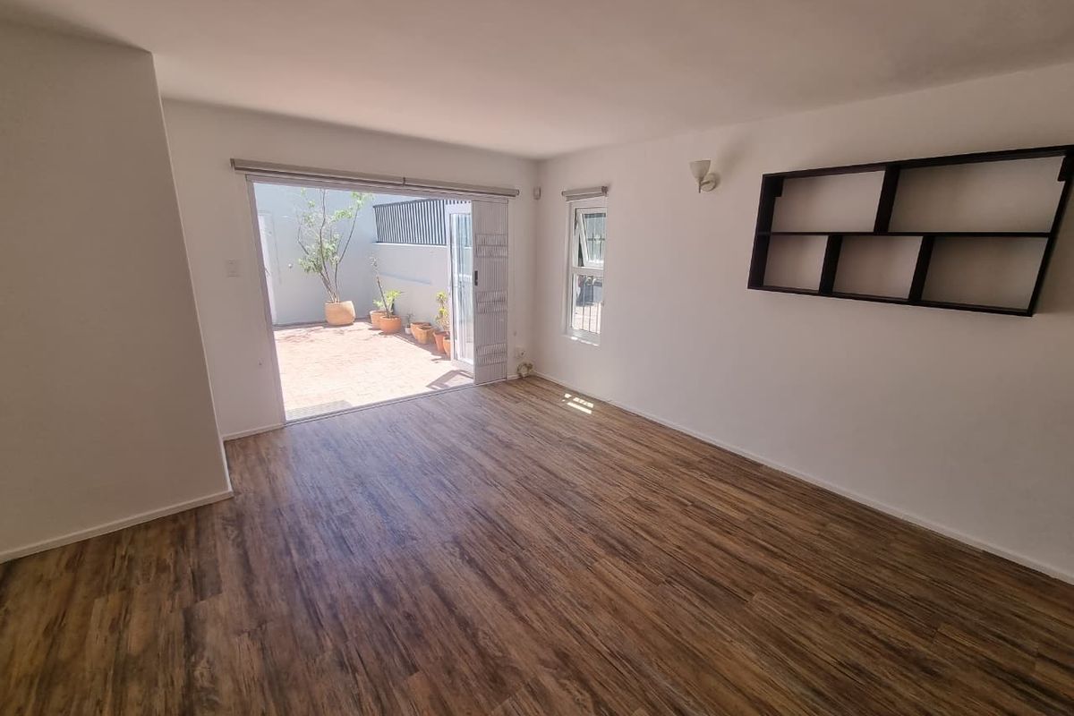 Bright and spacious living area featuring durable laminate flooring, built-in wall shelving, and direct access to an outdoor patio through sliding glass doors.