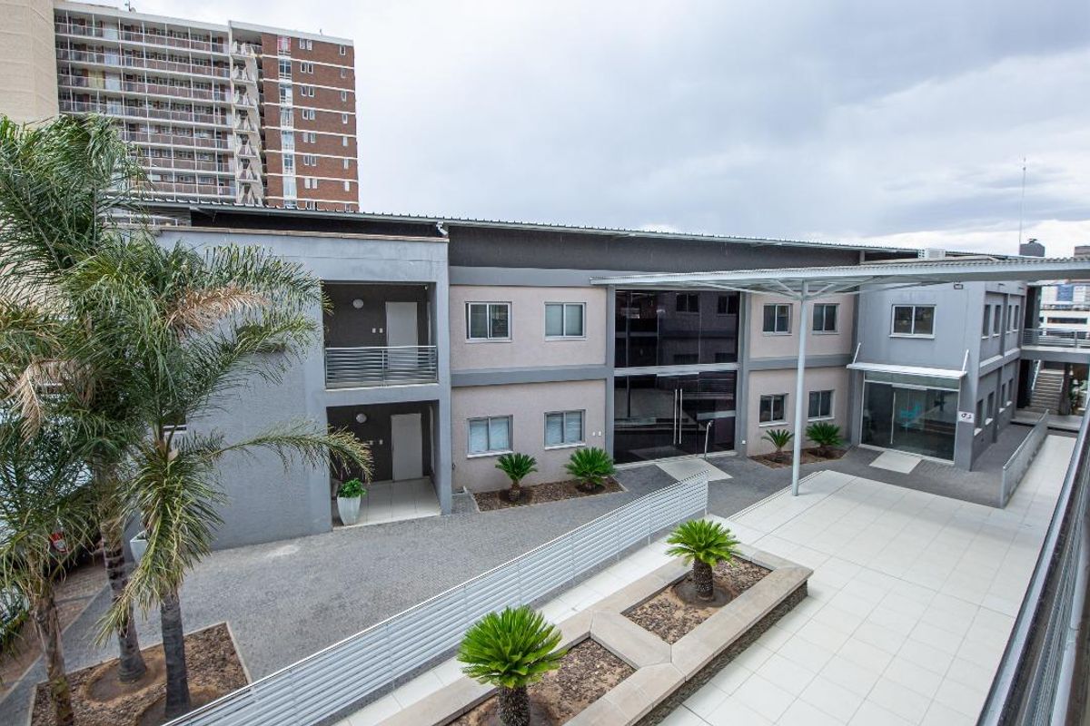 Elevated view of a modern office building exterior featuring a paved courtyard, covered walkway, and landscaped garden beds.