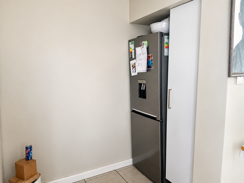 A kitchen corner featuring a built-in pantry cupboard with a sleek white finish and tiled flooring.