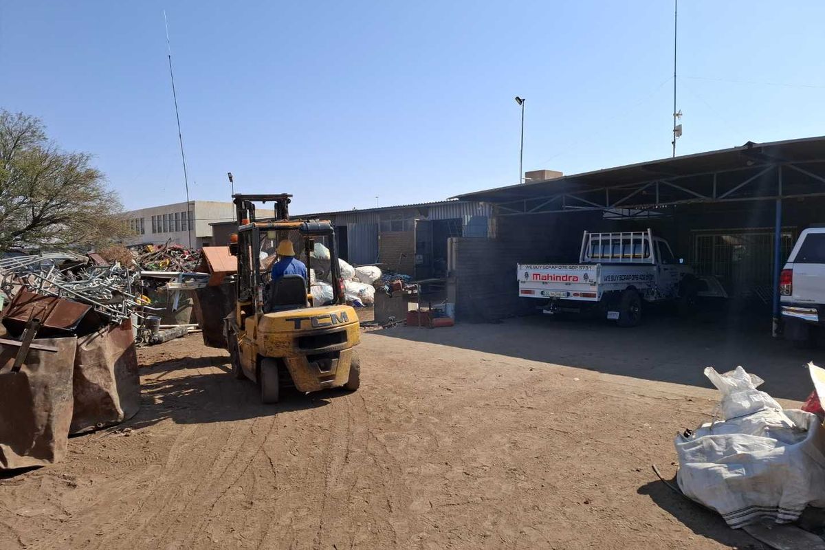 Industrial yard area featuring a covered loading bay, metal storage structures, and an unpaved ground surface suitable for heavy-duty business operations.