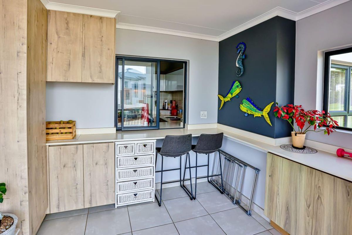 A modern kitchen area featuring light wood-finish cabinetry, laminate countertops, tiled flooring, and a convenient serving window connecting to the adjacent space.
