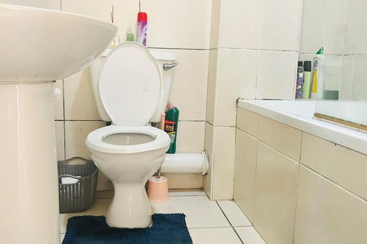 A compact bathroom featuring a pedestal basin, standard toilet, and a bathtub with a glass shower screen, finished with neutral wall and floor tiling.