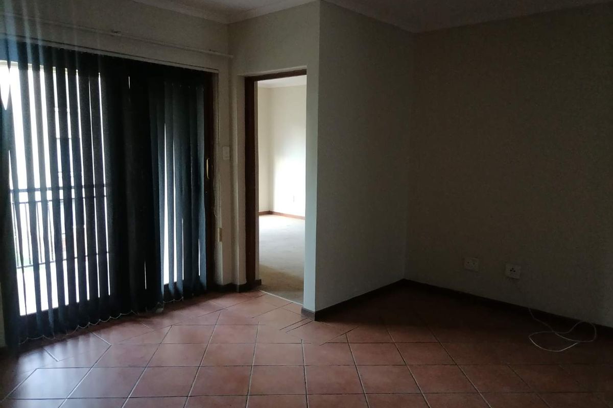 An empty living area featuring terracotta floor tiles and a sliding glass door leading to an outdoor space, with an adjacent room visible.