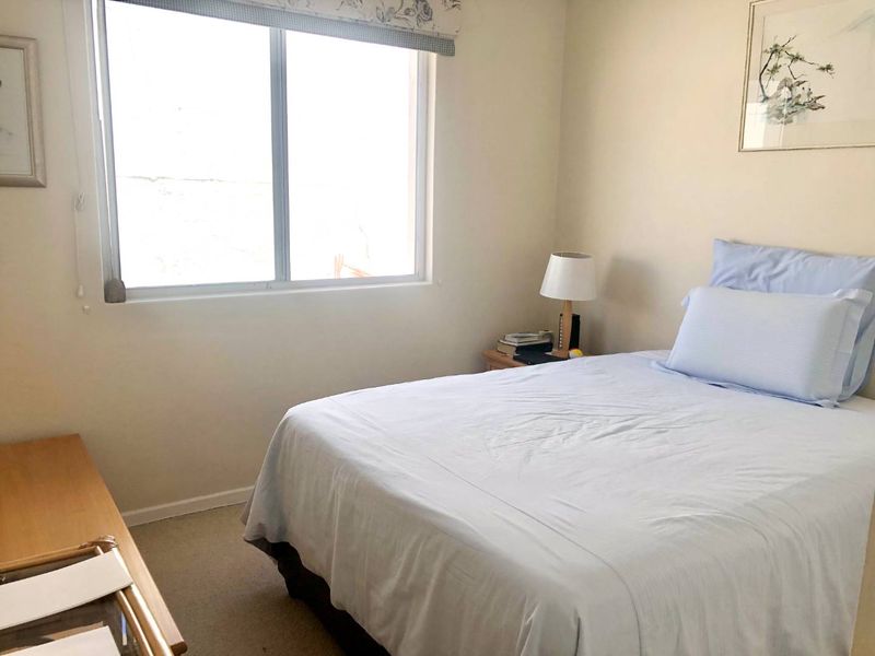 A standard bedroom featuring neutral wall finishes, carpeted flooring, and a sliding window providing natural light.