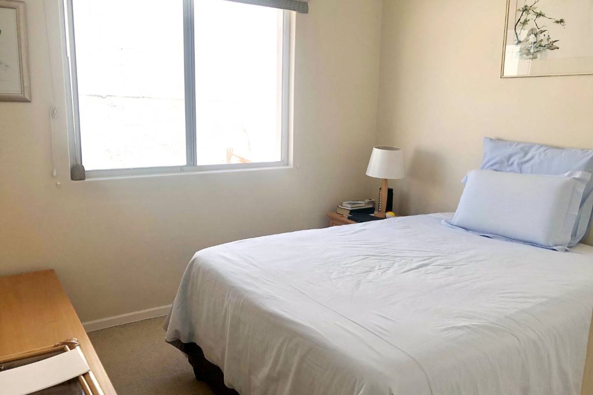 A standard bedroom featuring neutral wall finishes, carpeted flooring, and a sliding window providing natural light.