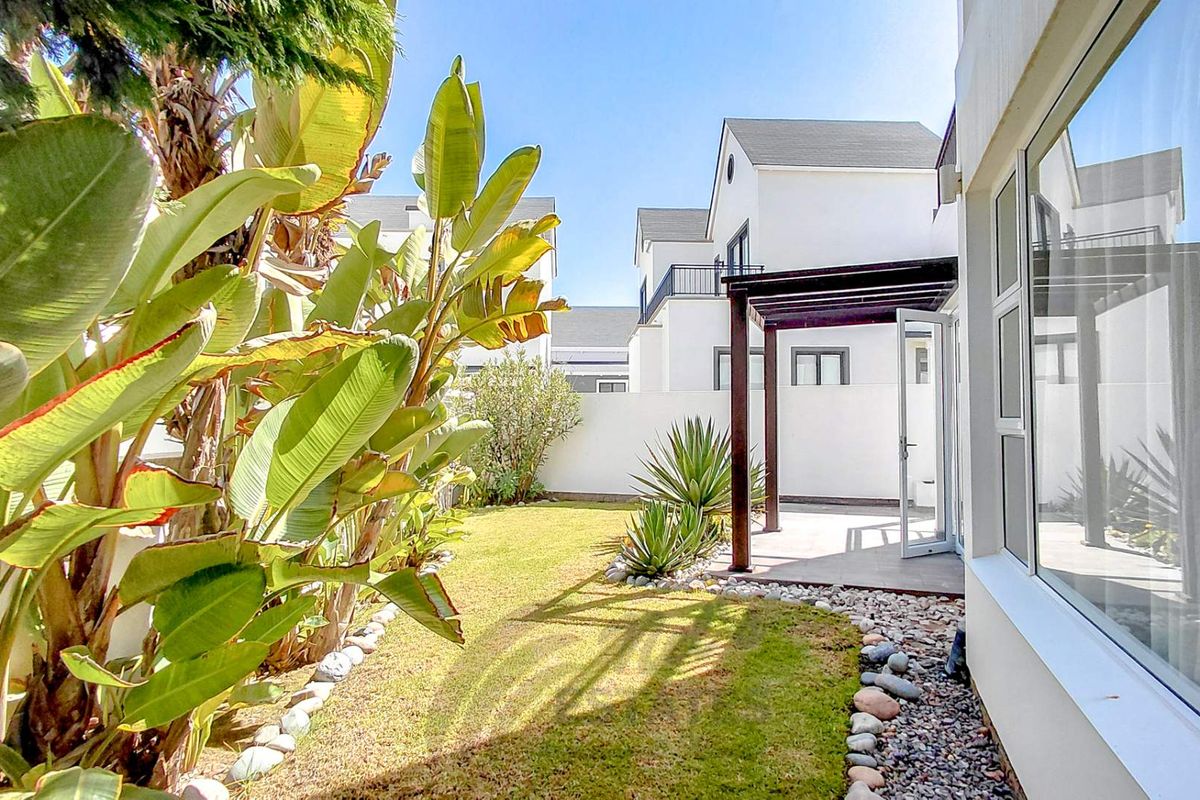 A well-maintained rear garden featuring a paved patio area with a timber pergola, manicured lawn, and established landscaping adjacent to the townhouse structure.