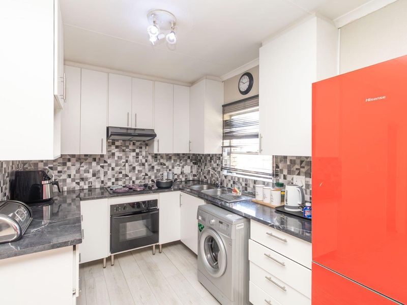 A functional kitchen featuring white cabinetry, dark laminate countertops, a tiled backsplash, and integrated appliances including an oven and hob.