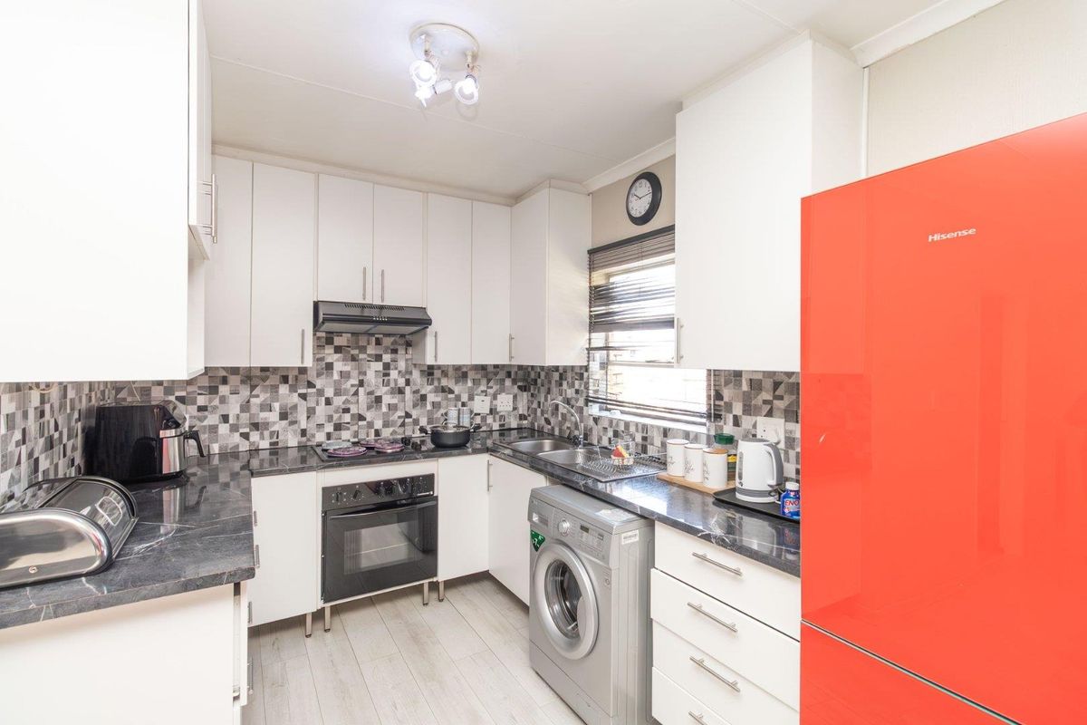 A functional kitchen featuring white cabinetry, dark laminate countertops, a tiled backsplash, and integrated appliances including an oven and hob.