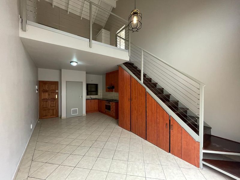 Open-plan living area featuring a kitchen with built-in cabinetry, under-stair storage, and a mezzanine level with a metal balustrade.