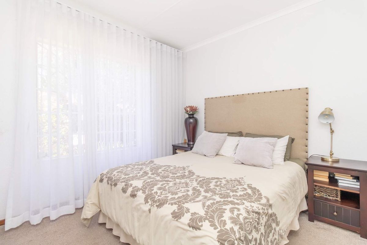 A well-lit bedroom featuring neutral carpet flooring, coved ceilings, and large windows dressed with sheer curtains.
