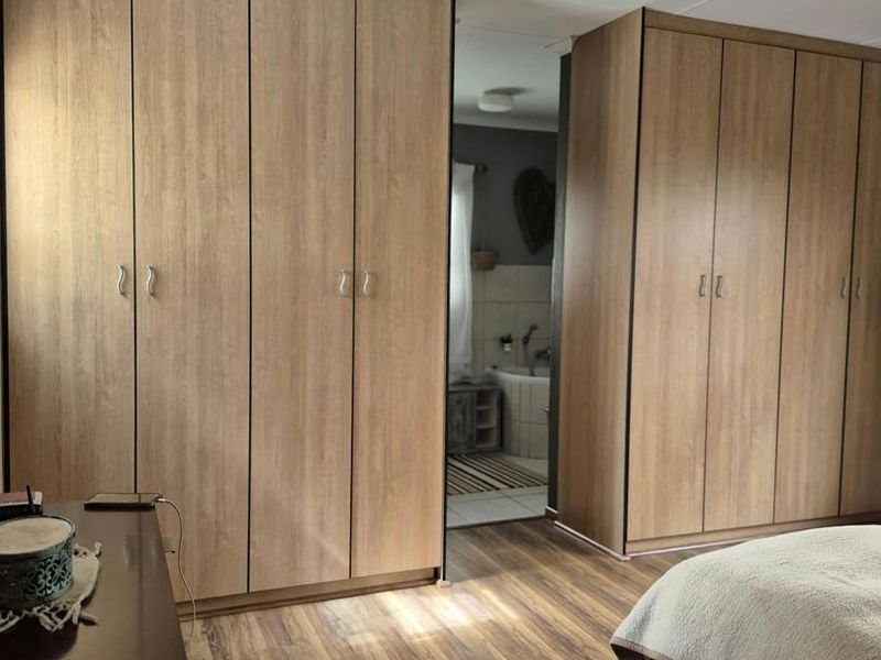 A bedroom featuring extensive built-in wooden wardrobes and durable laminate flooring, with an adjoining view into a bathroom area.