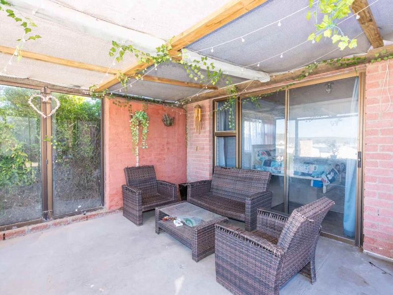 Covered outdoor patio area featuring exposed brick walls, concrete flooring, and a timber pergola structure with shade cloth, providing direct access to the interior.
