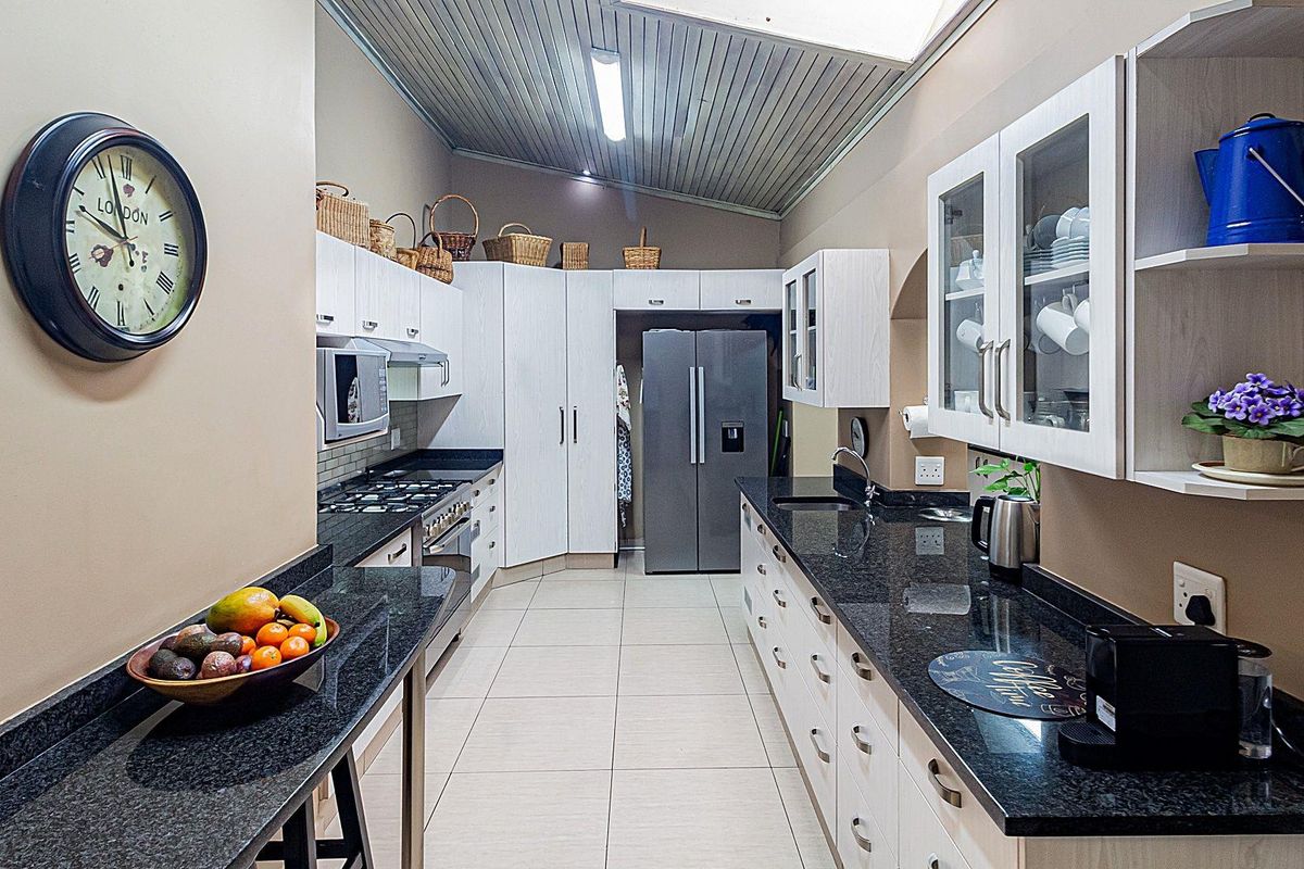 A functional galley-style kitchen featuring granite countertops, light-toned cabinetry, a gas hob, and tiled flooring under a vaulted ceiling.
