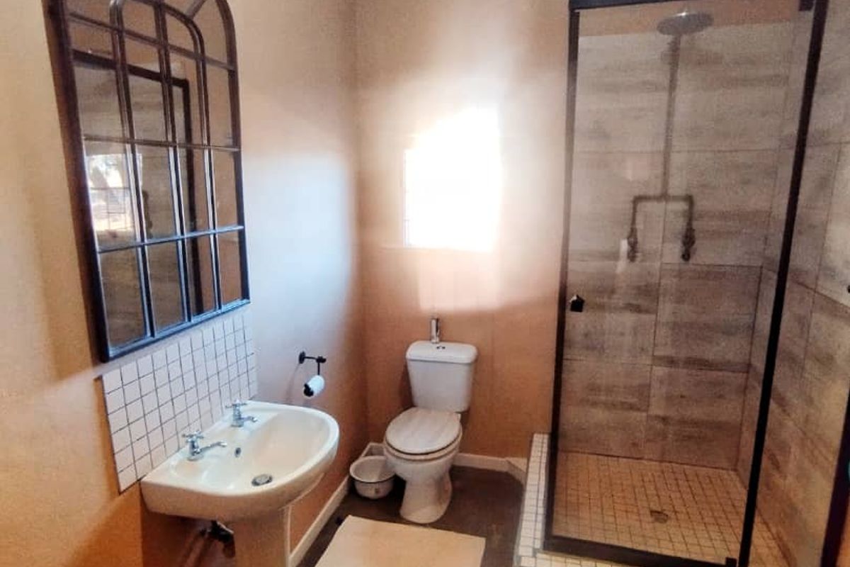 A functional bathroom featuring a pedestal basin, a toilet, and a glass-enclosed shower with tiled surrounds.