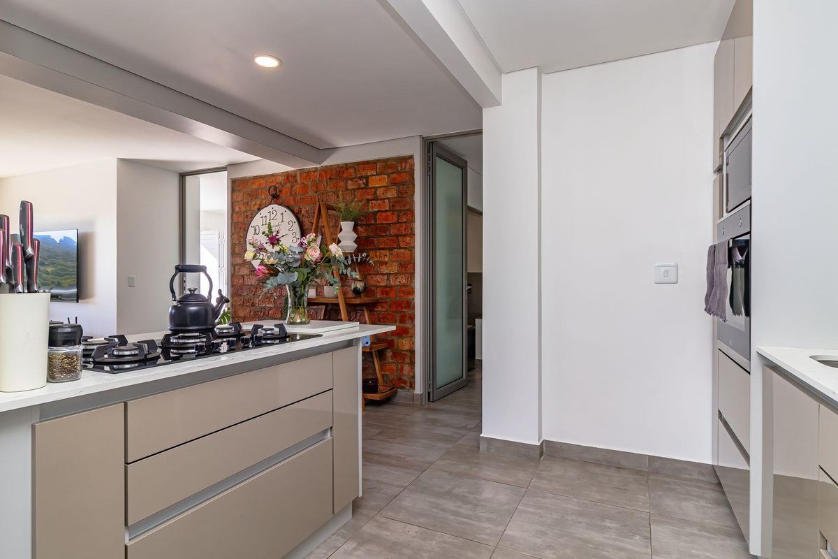 Modern kitchen featuring a central island with a built-in gas hob, sleek cabinetry, and a distinctive exposed brick feature wall.