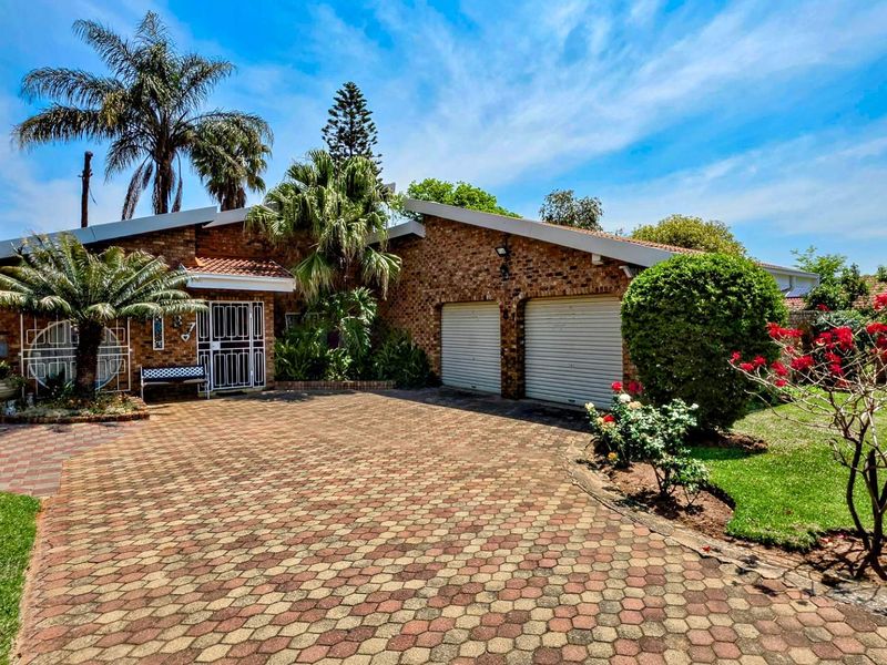 Front view of a face brick house featuring a double garage, paved driveway, and established garden.